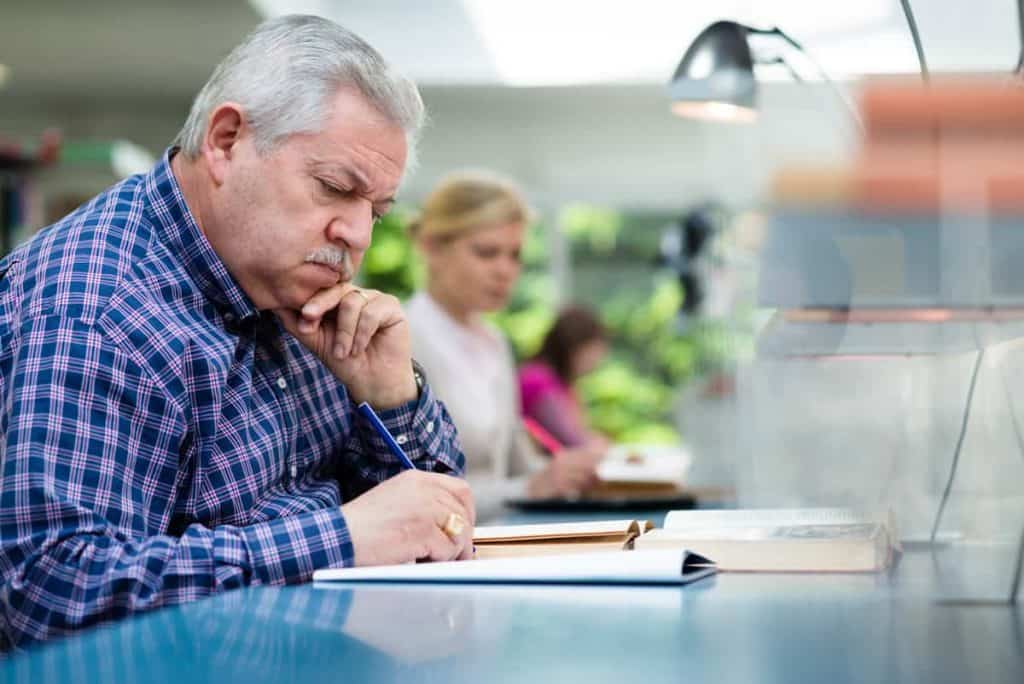 Ein älterer Herr sitzt stirnrunzelnd über Formularen