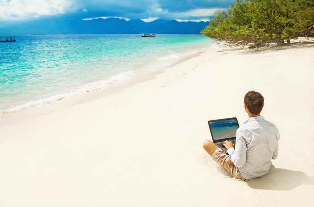 Ein Digitalnomade sitzt am Strand und arbeitet am Laptop